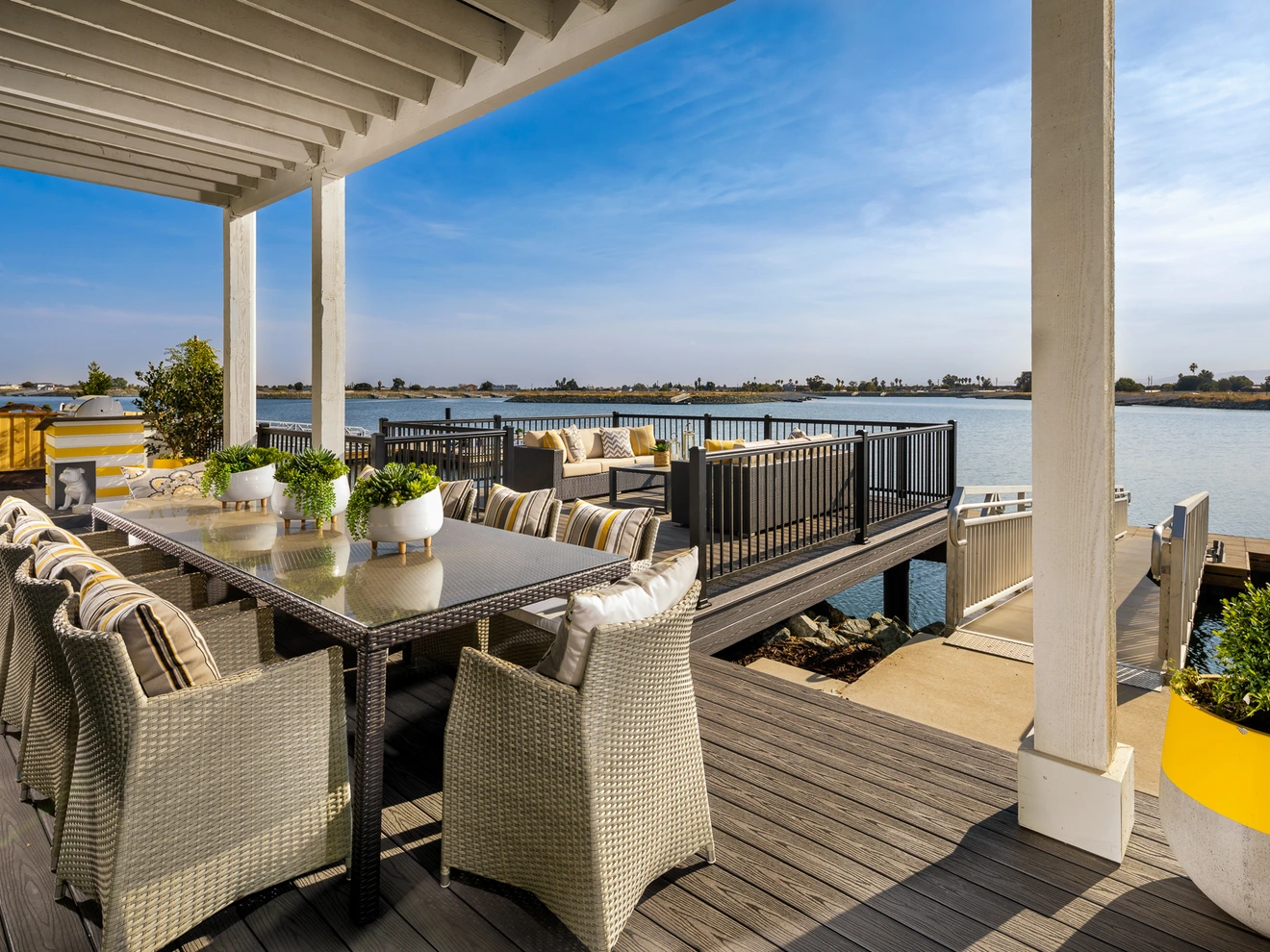 Outdoor patio with dining table, wicker chairs, seating area, and waterfront view under clear sky.