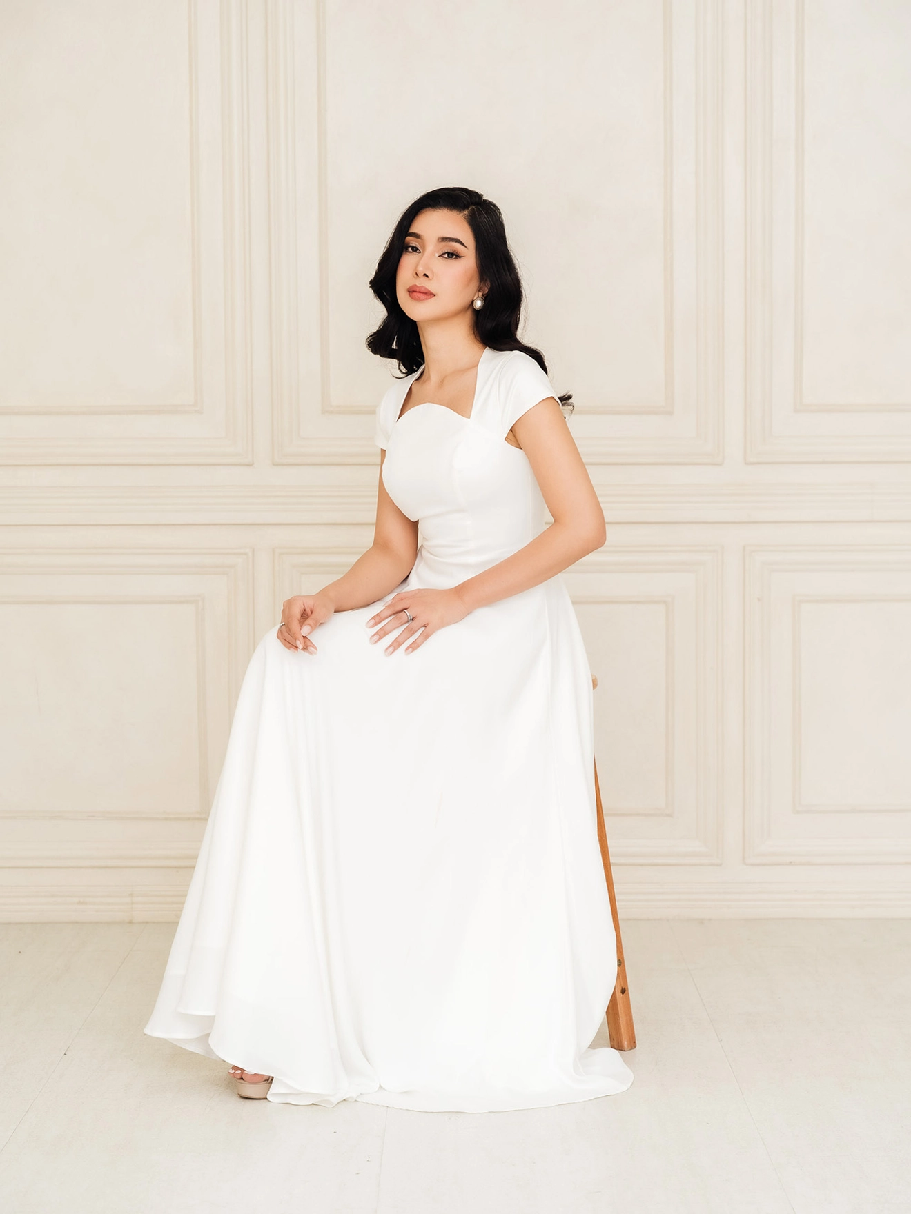 Woman posing on a stool wearing a white dress.