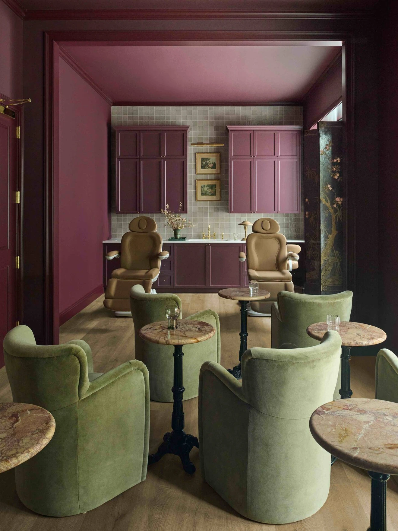 Room with green armchairs, small round tables, and a purple-themed corner with cabinets and chairs.
