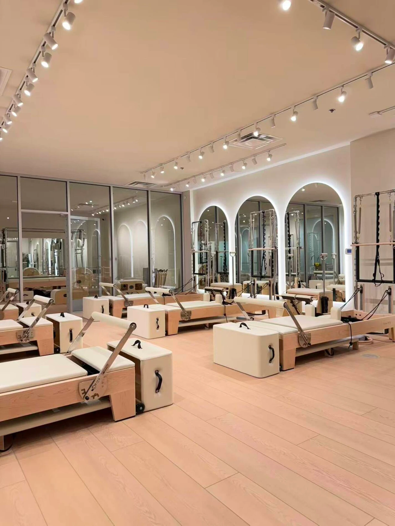 Spacious Pilates studio with reformer machines, wooden flooring, large mirrors, and soft overhead lighting.