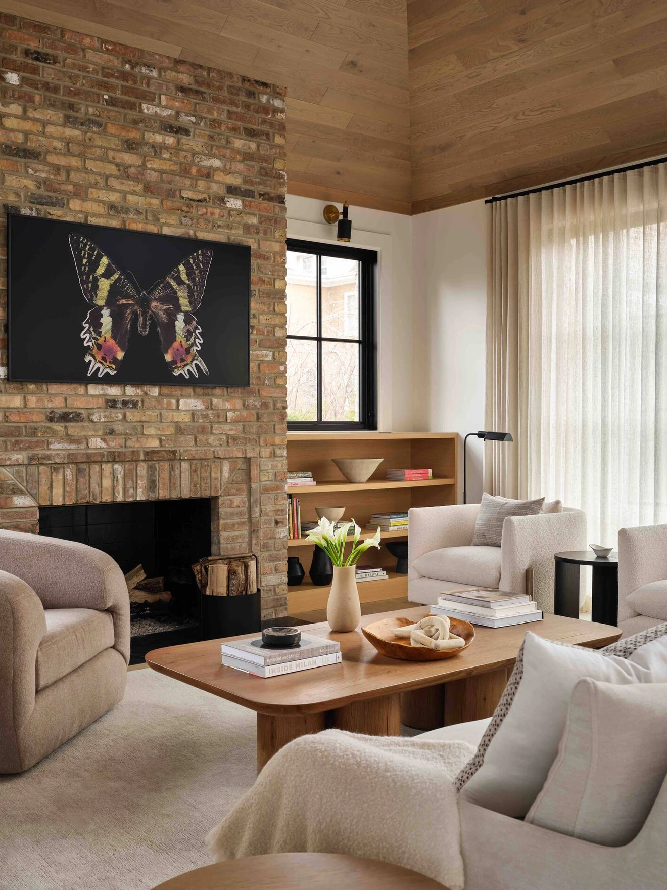 Cozy living room with brick fireplace, butterfly artwork, neutral furniture, wooden coffee table, and natural light.