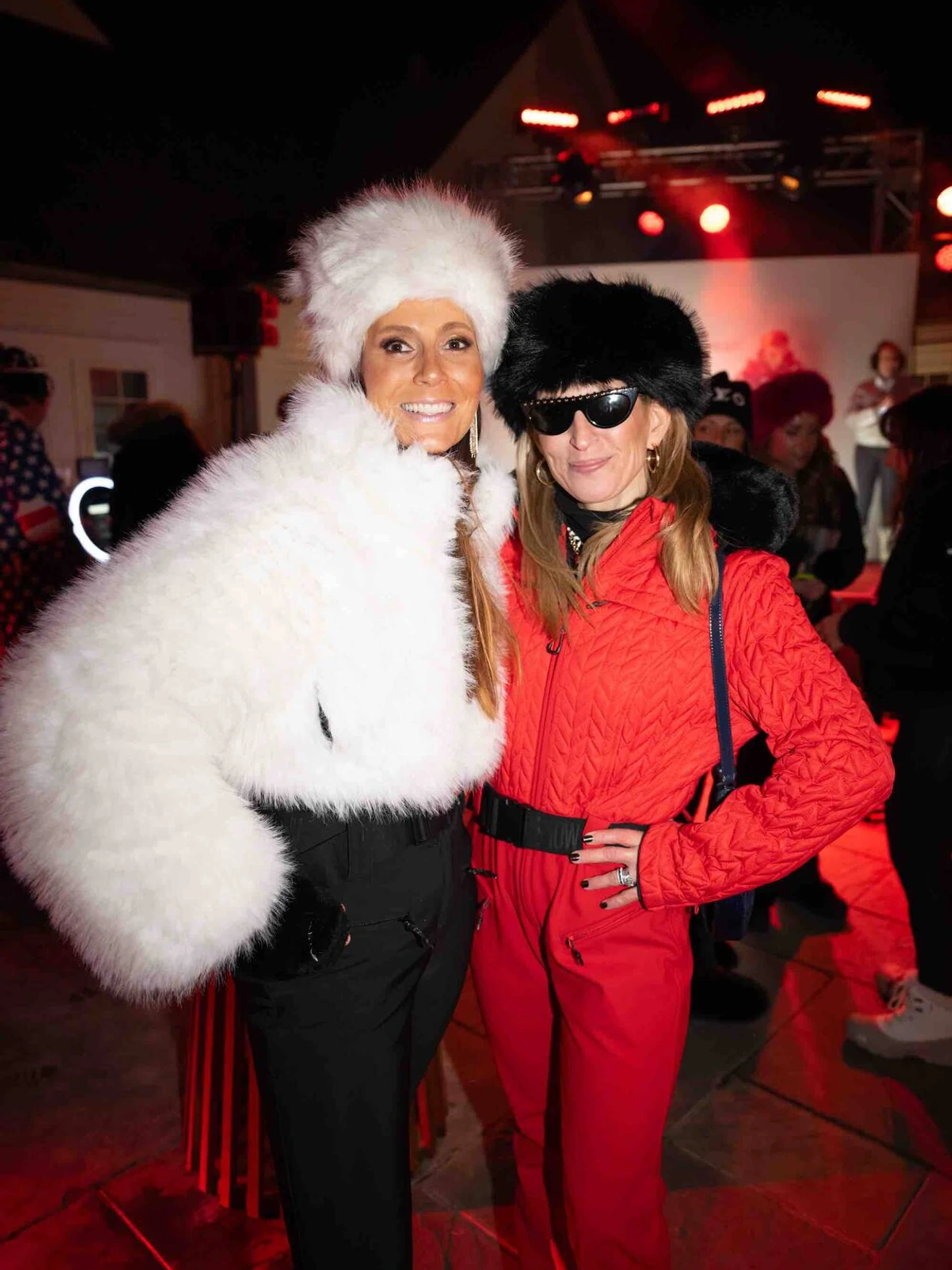 Two women dressed in winter clothing, one in white fur, the other in red outfit and black fur hat.