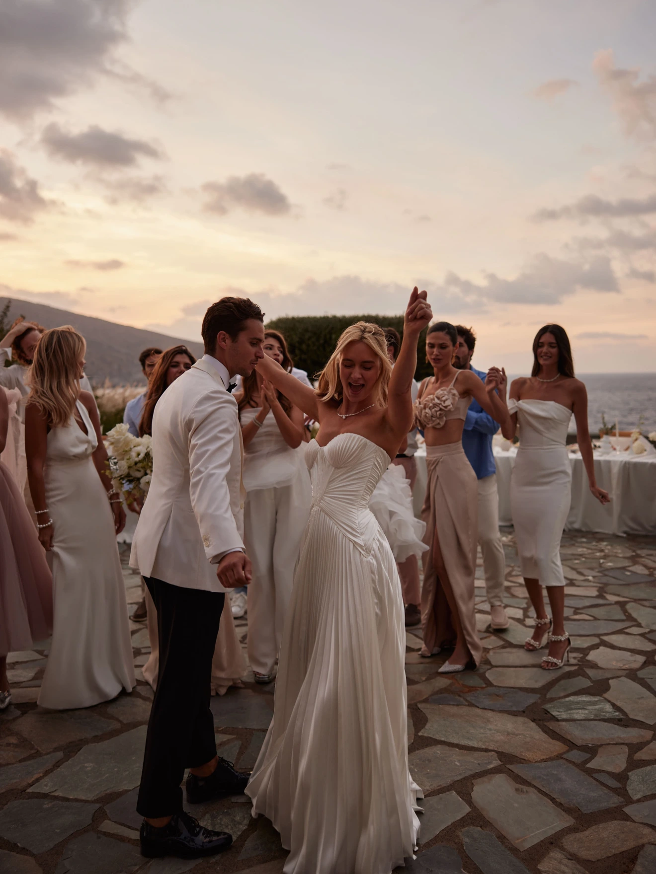 Bride and groom dancing outdoors during sunset, surrounded by bridesmaids in elegant dresses.