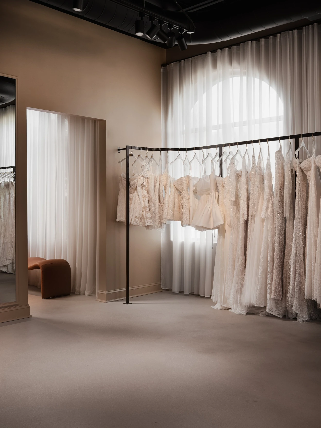 Elegant bridal boutique with white wedding dresses hanging on a black clothing rack near sheer curtains.