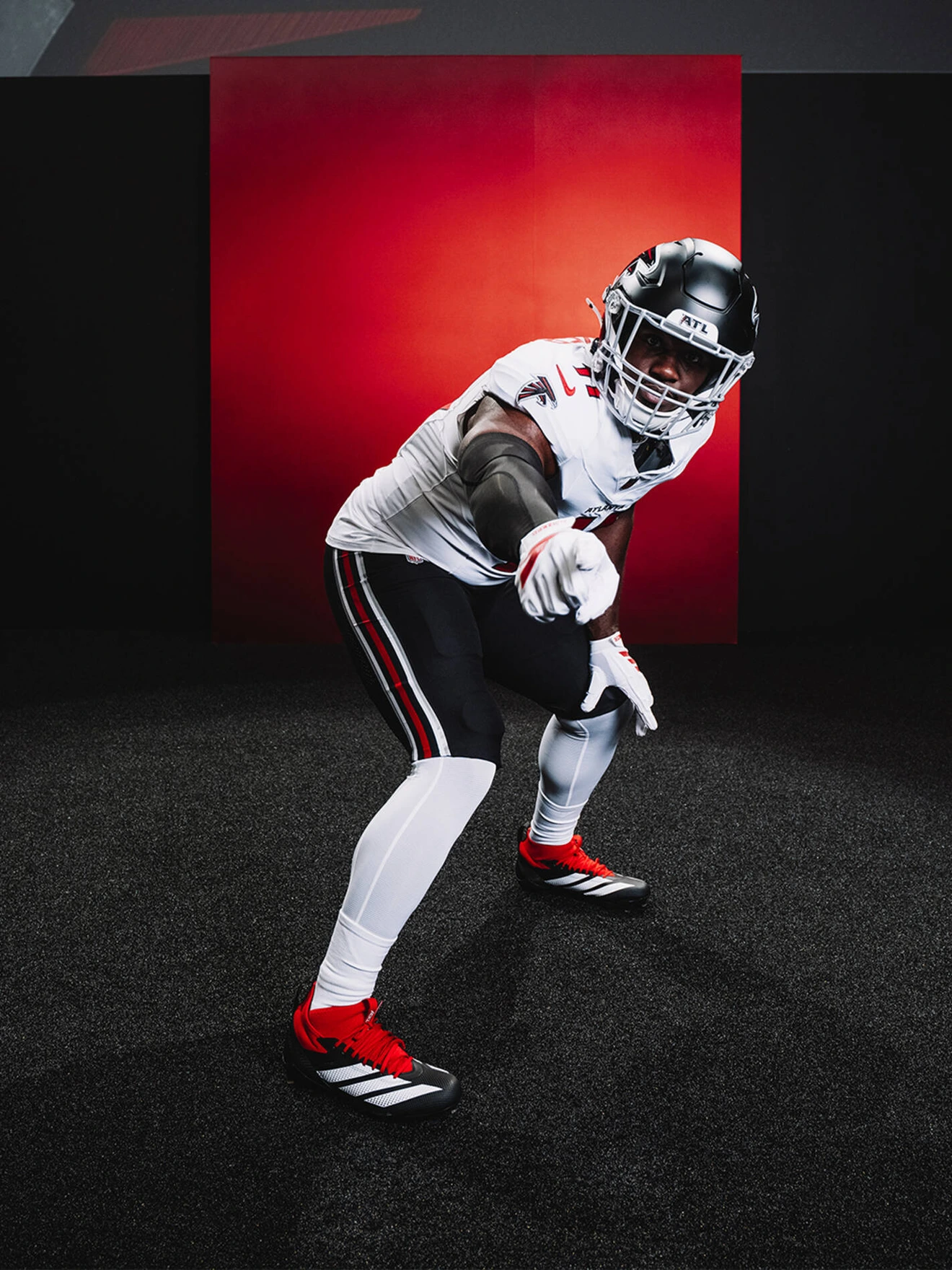 American football player in white Tampa Bay Buccaneers uniform pointing forward against red background.