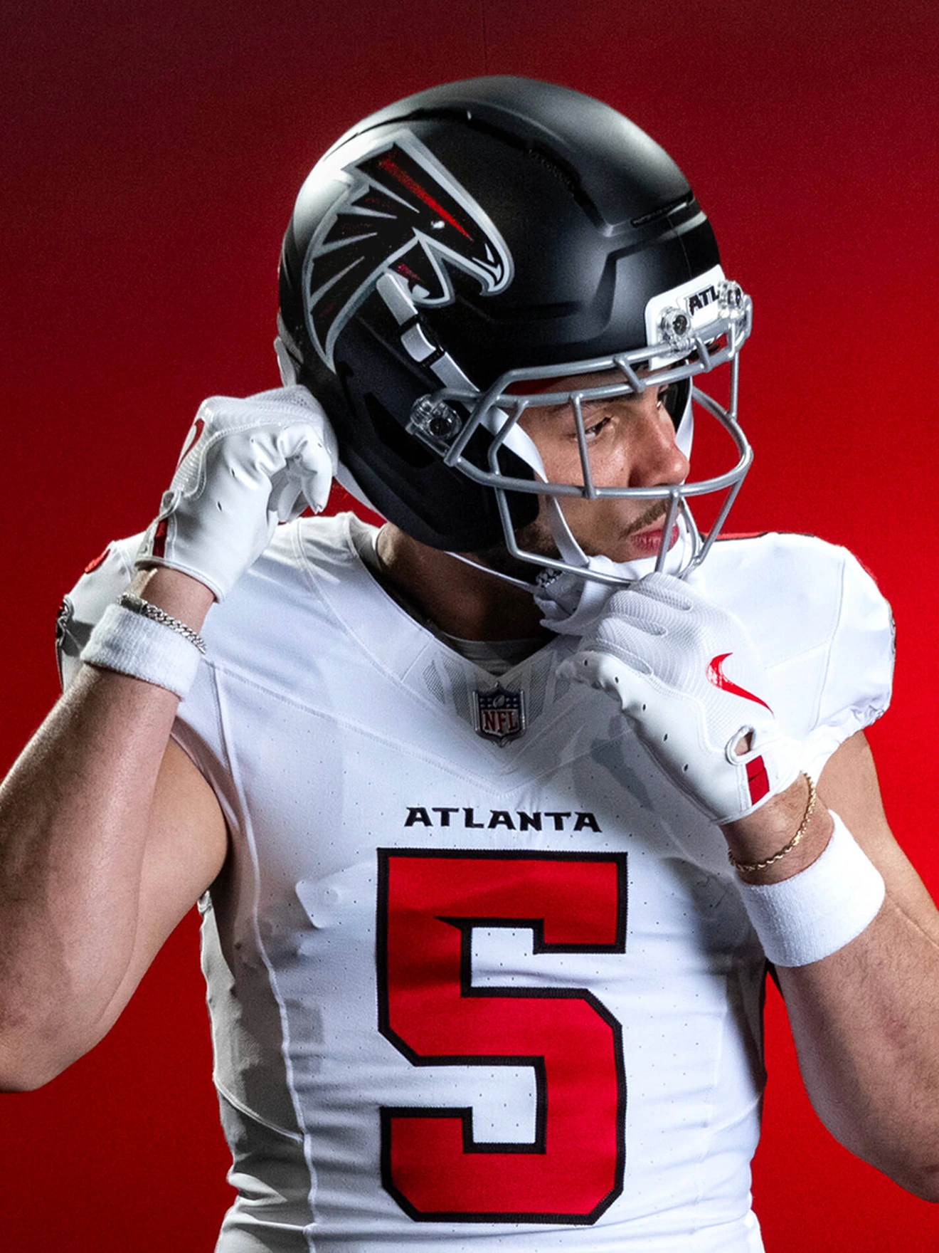 Atlanta Falcons football player adjusting helmet, wearing white jersey number 5, red background.