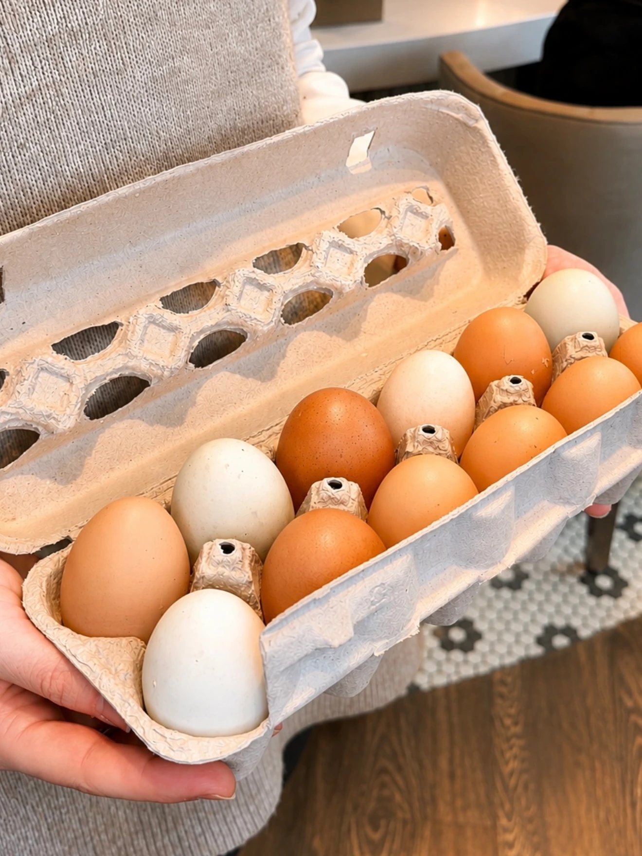 Person holding an open carton with a mix of brown and white eggs inside.