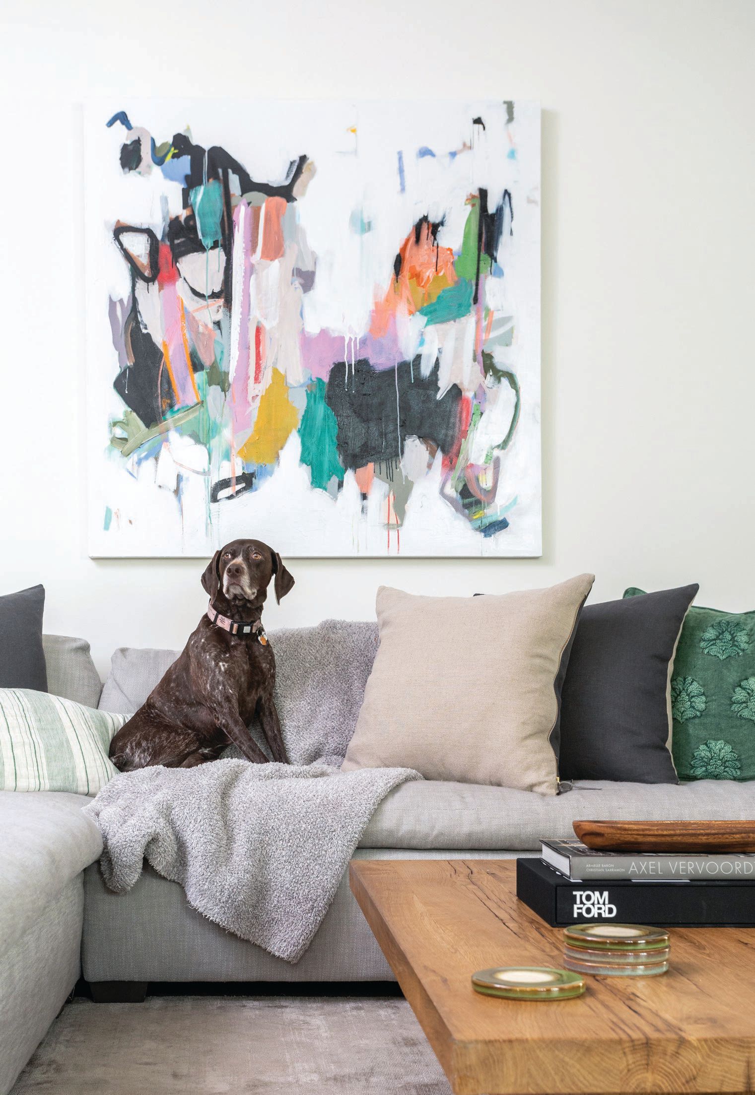 The living room features a standout art piece by local artist Annie King. Here, the couple’s German shorthaired pointer poses comfortably on the sectional from CB2, near the coffee table by Restoration Hardware. PHOTOGRAPHED BY HEIDI HARRIS