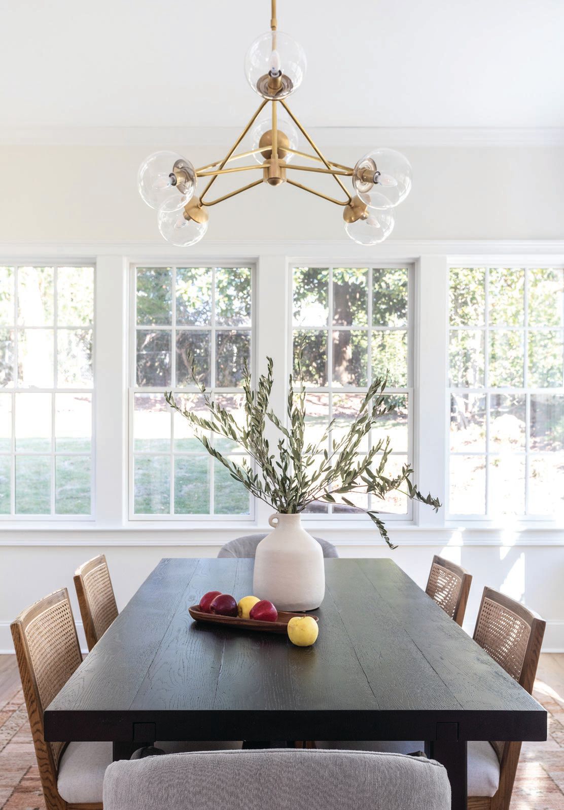 The dining room features a chandelier by Visual Comfort, a Restoration Hardware dining table, France & Son head dining chairs, Four Hands dining chairs and buffet, an area rug by Jaipur Living and artwork by Lindsey J. Porter. PHOTOGRAPHED BY HEIDI HARRIS