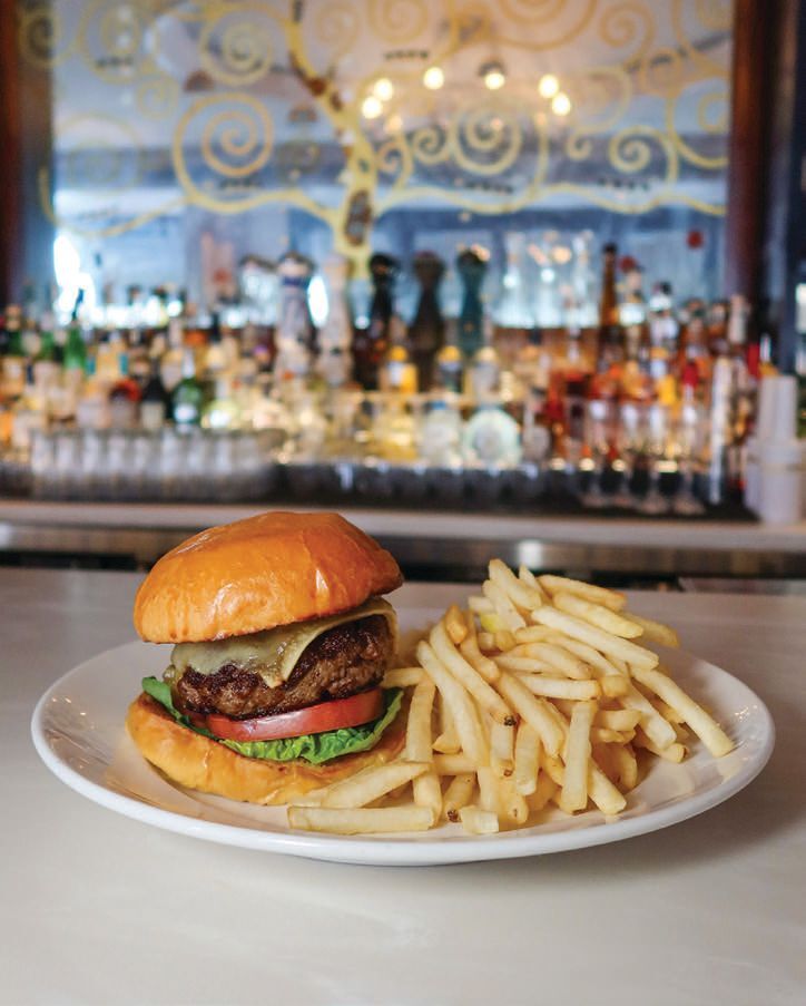 A cheeseburger with lettuce, tomato, and French fries on a plate, with a bar in the background.