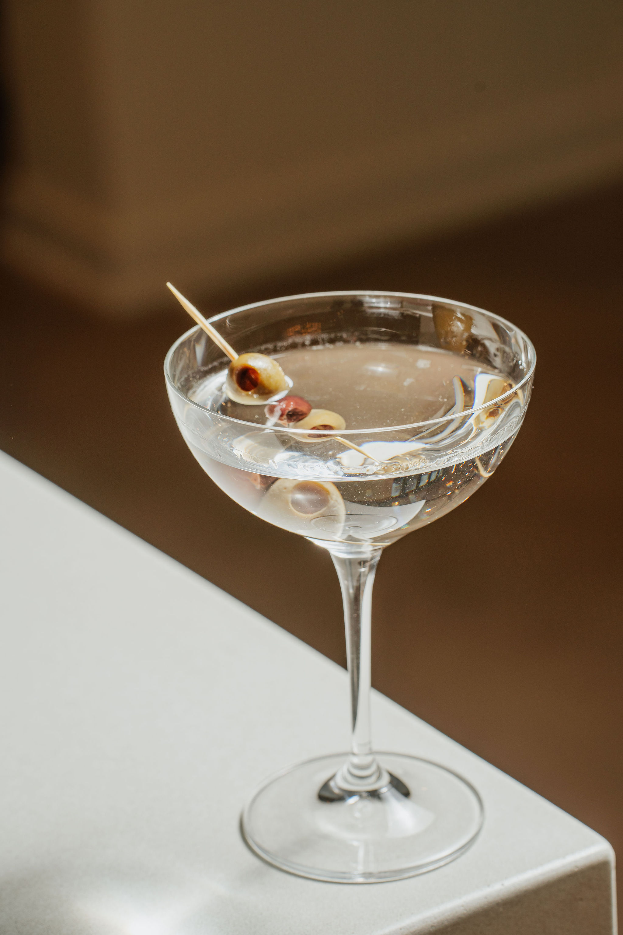 A martini glass filled with a clear drink and olives on a toothpick.