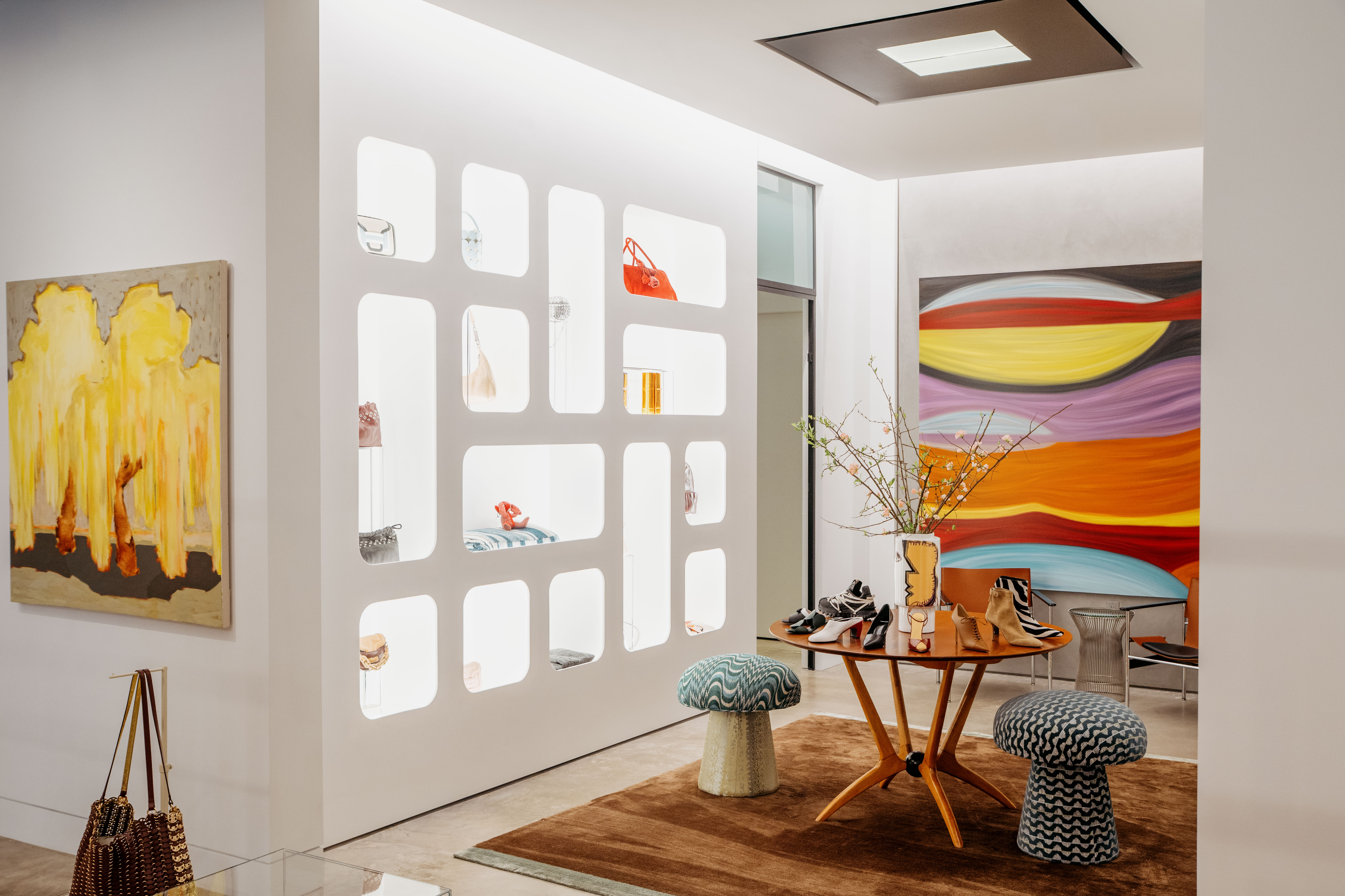 Modern boutique interior with illuminated shelves, colorful abstract paintings, and stylish furniture.