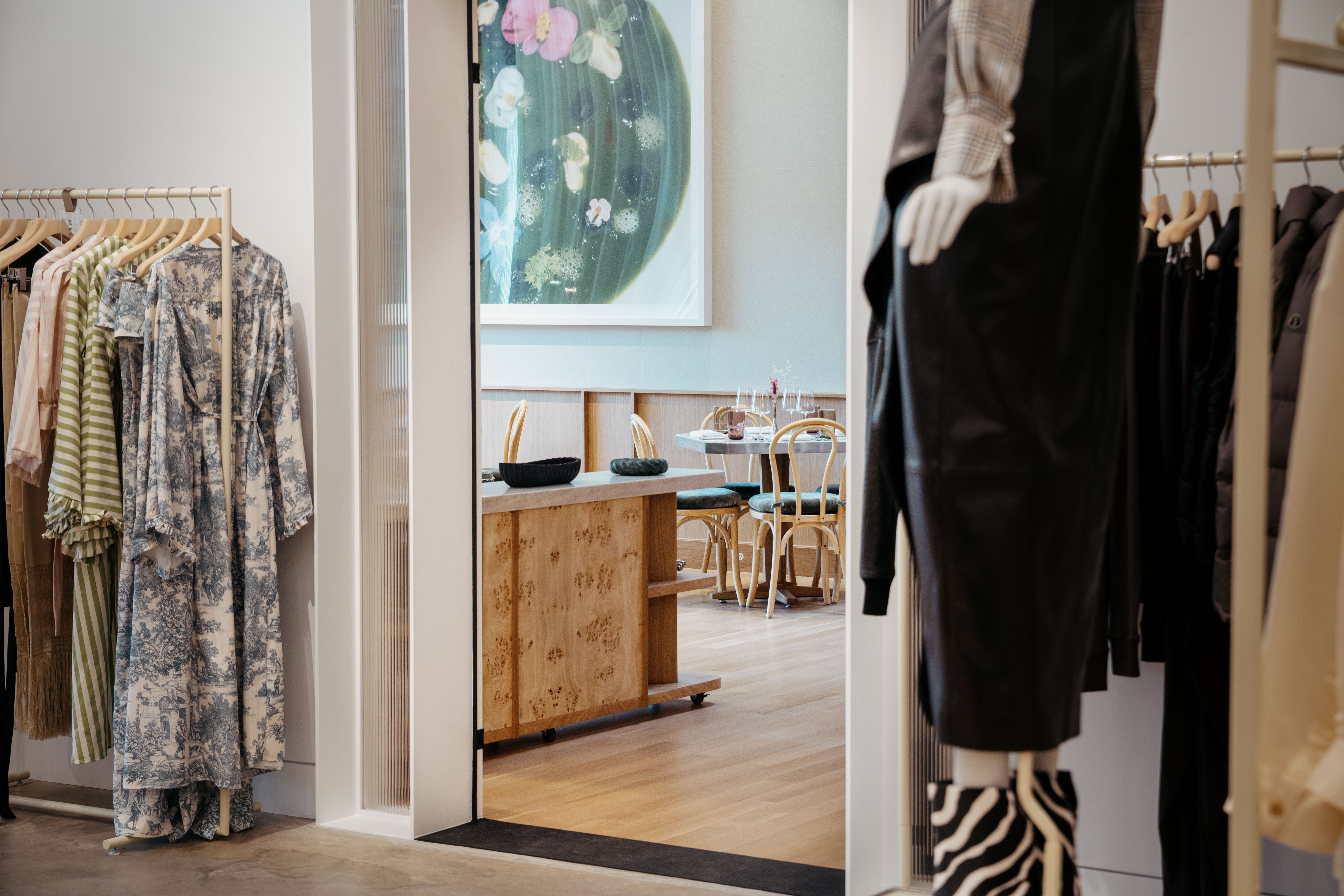 Boutique interior with clothing racks, mannequins, wooden furniture, and a floral artwork on the wall.