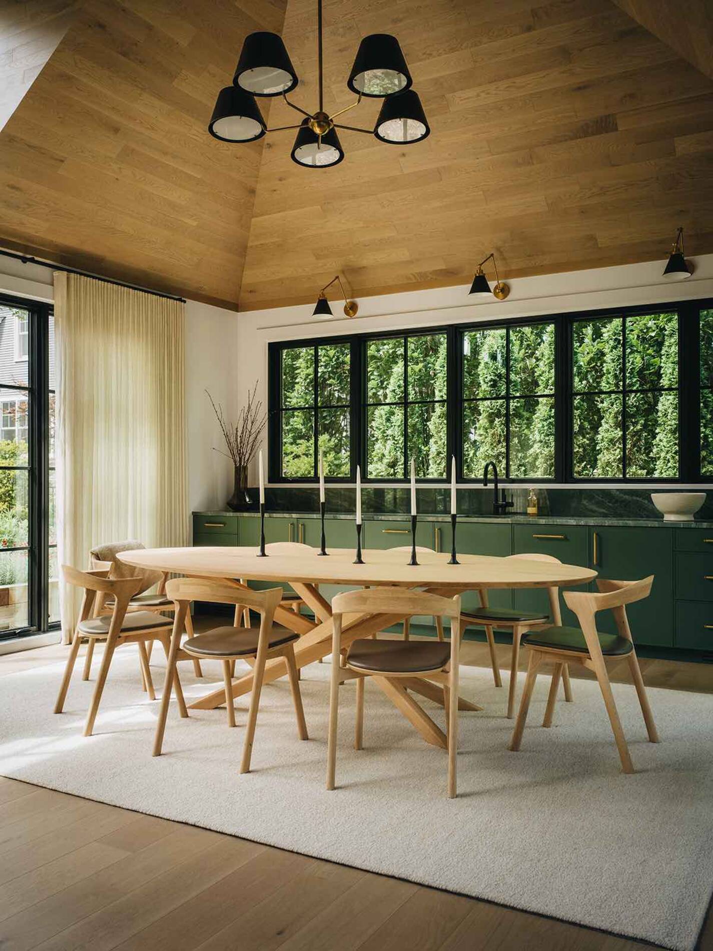 Modern dining room with wooden table and chairs, large black-framed windows, and a vaulted wooden ceiling.