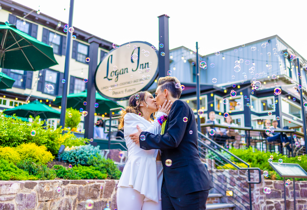 Couple sharing a kiss outdoors near Logan Inn sign with bubbles floating around.