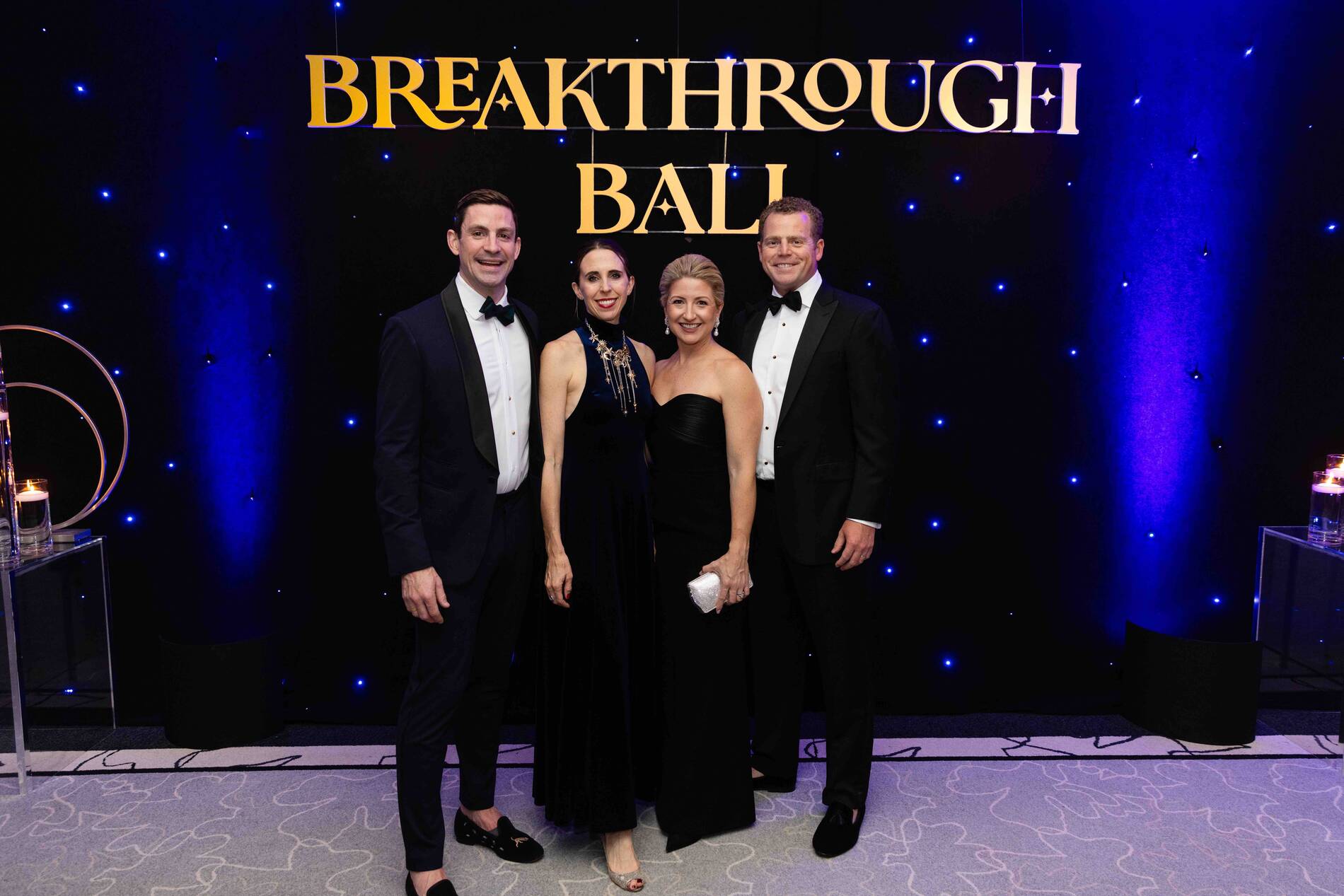 Four people dressed formally posing at the Breakthrough Ball event with a dark starry background.
