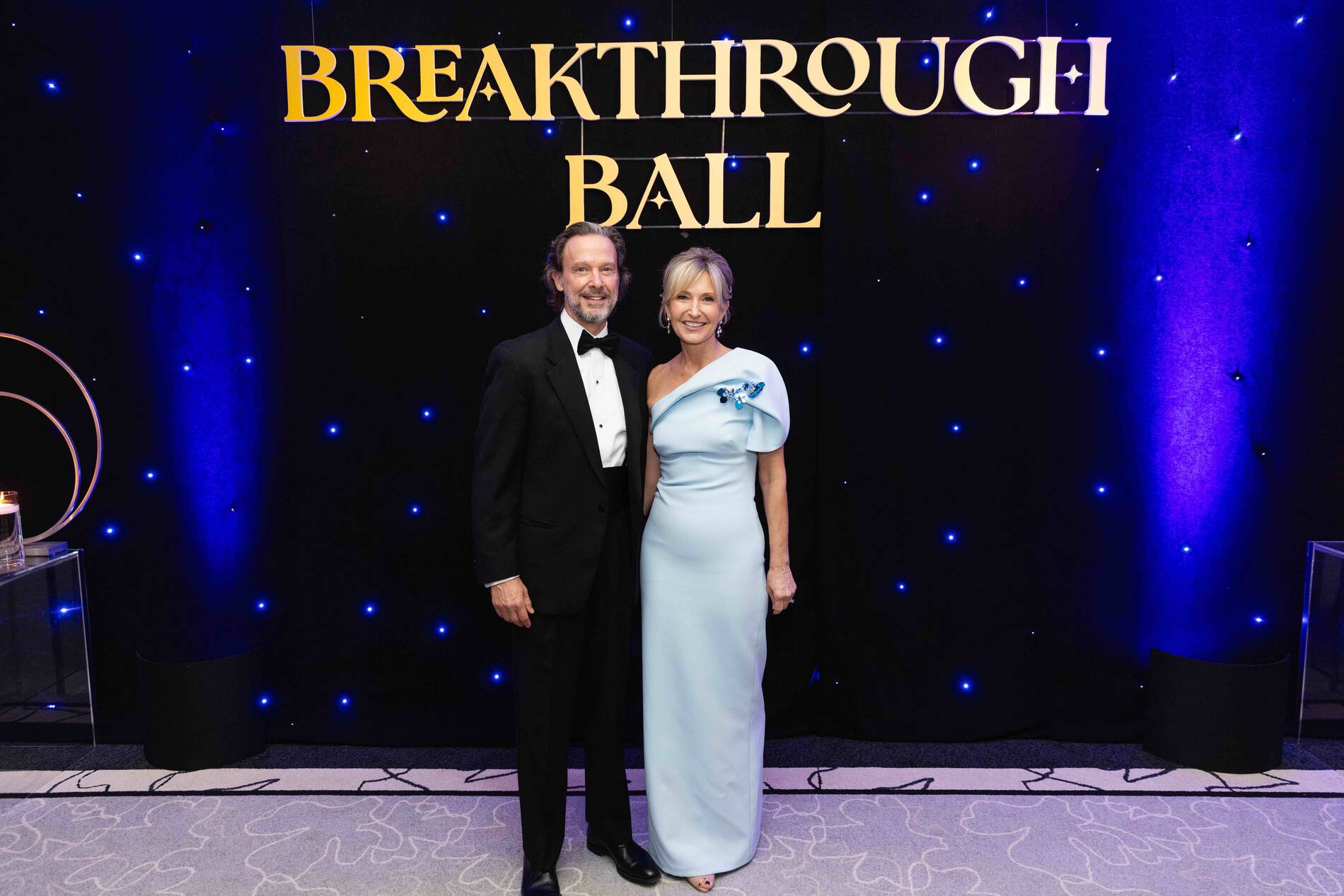 Man in tuxedo and woman in light blue gown posing at Breakthrough Ball event.