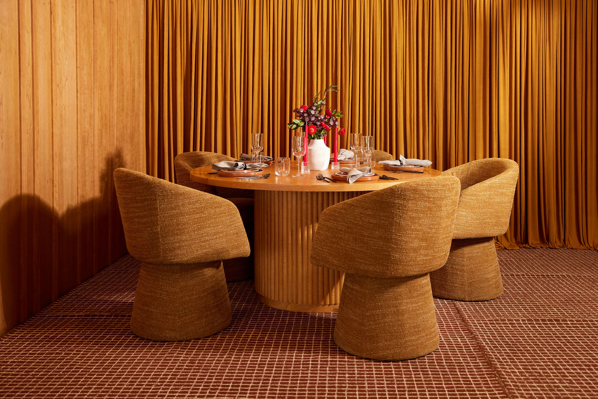 Round wooden dining table with four mustard-colored chairs and flower centerpiece in a warm-toned room.