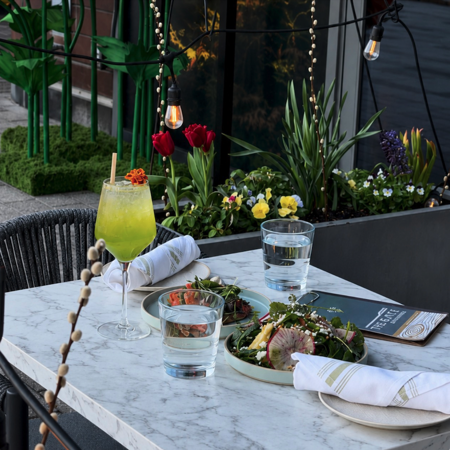Outdoor dining table with salad, green cocktail, water glasses, and floral decorations at a restaurant.