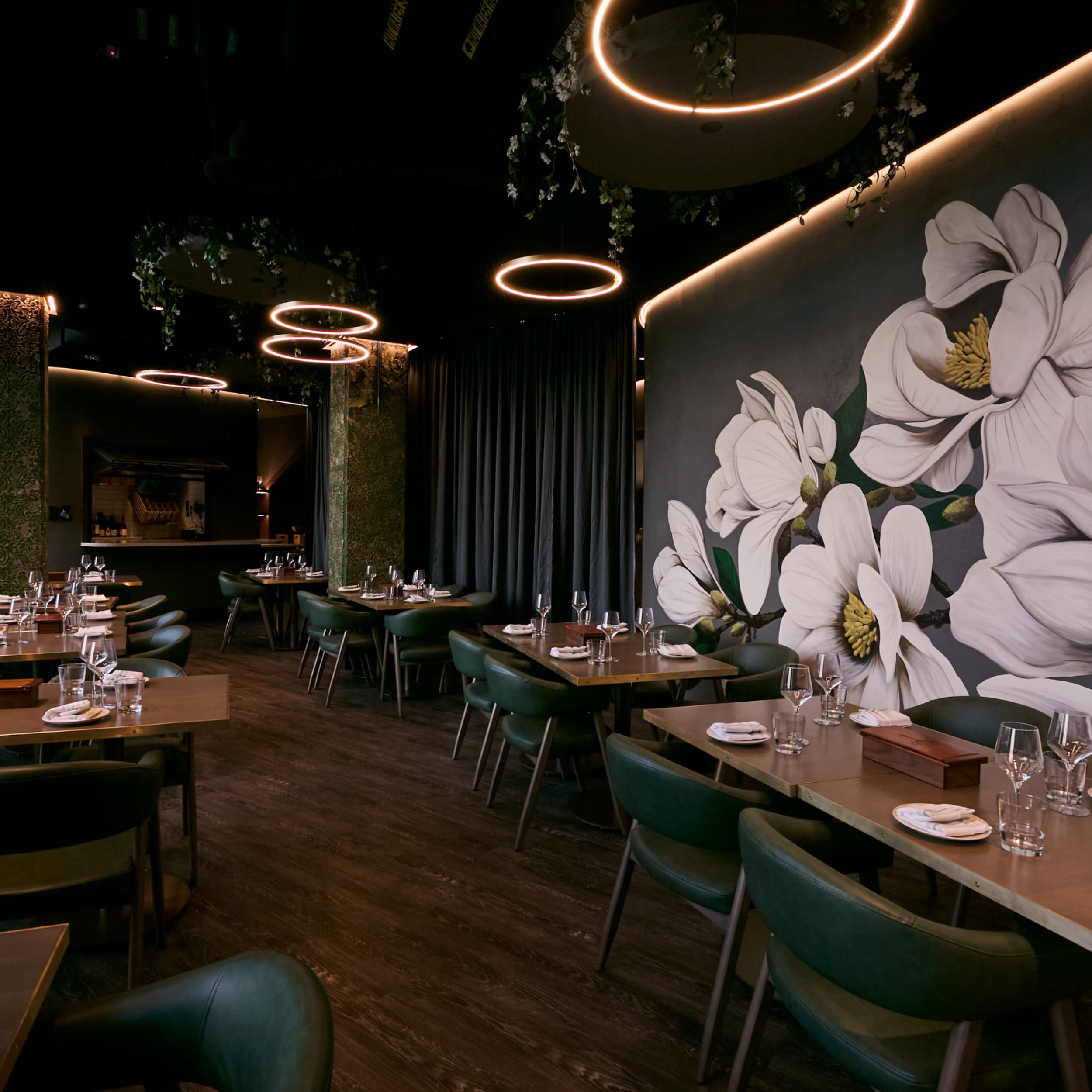 Modern restaurant interior with large white floral wall art, circular ceiling lights, and neatly set dining tables.