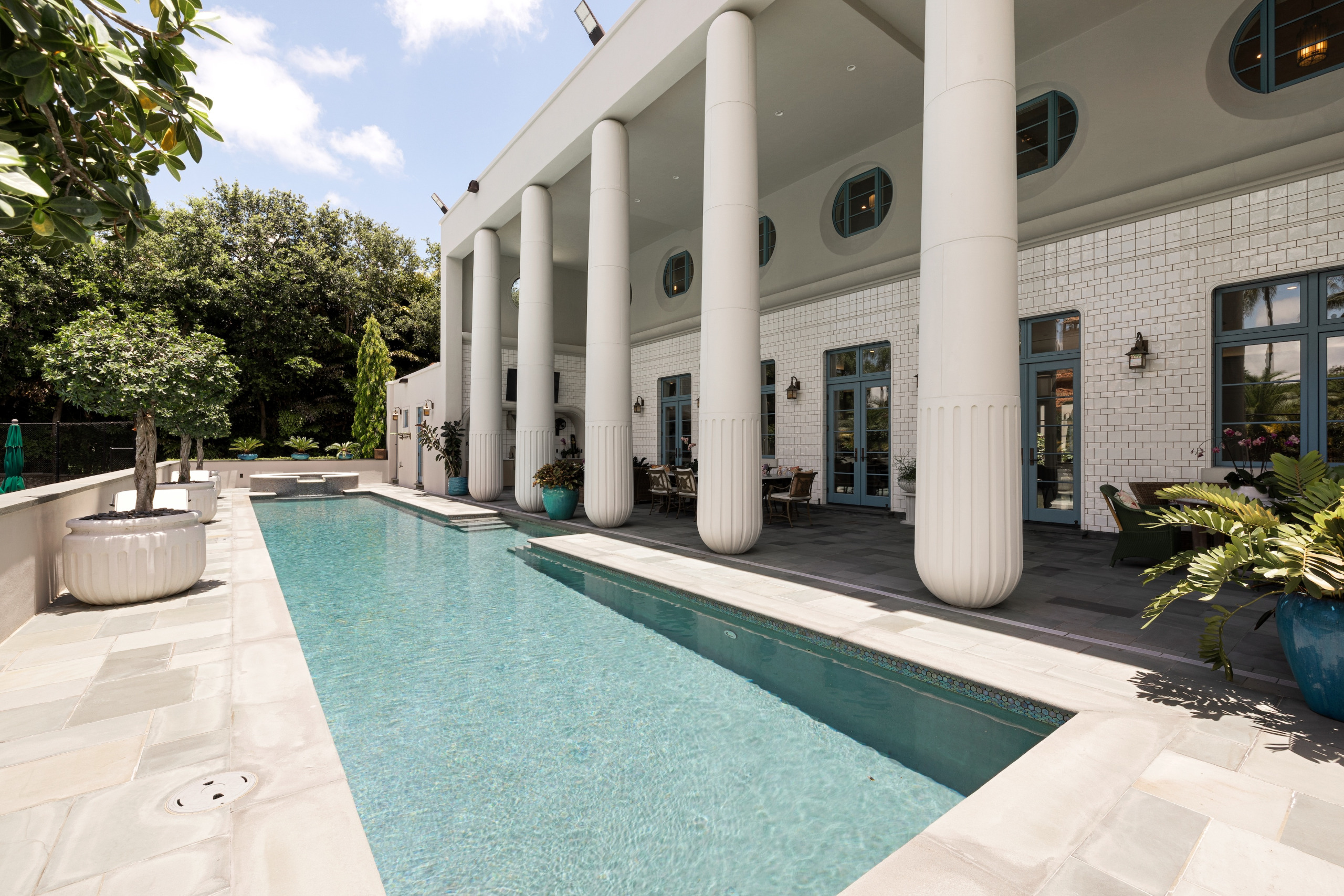 A modern pool area with columns, lounge chairs, and potted plants.