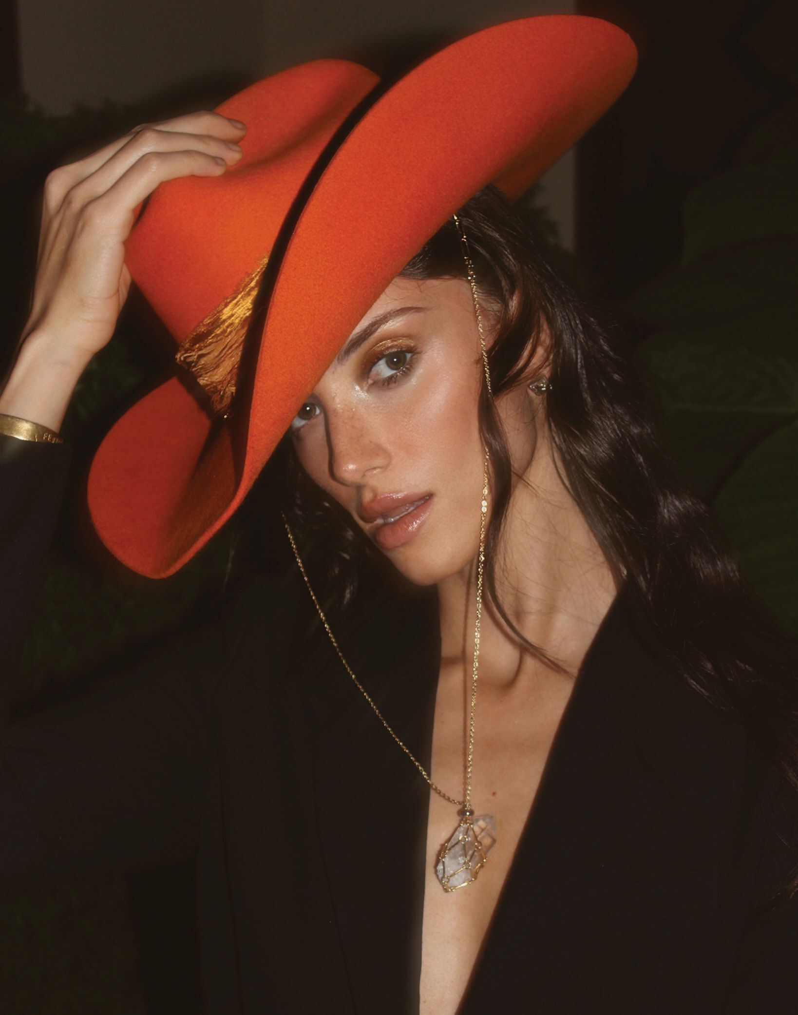 Nave wearing an orange wide-brimmed hat and black outfit, posing with hand touching the hat.